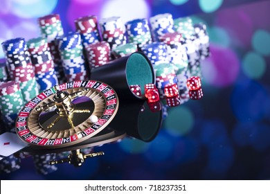 Casino theme. High contrast image of casino roulette, poker game, dice game, poker chips on a gaming table, all on colorful bokeh background. 
