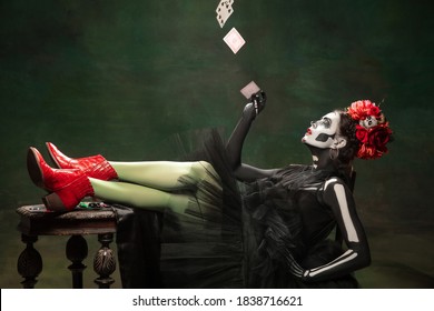 Casino. Young girl like Santa Muerte Saint death or Sugar skull with bright make-up. Portrait isolated on dark green studio background with copyspace. Celebrating Halloween or Day of the dead.