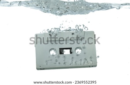 Cassette retro vintage Tape fall into clear water with air bubble. Black retro vintage cassette magnetic tape drop to wash old time. White background isolated freeze element