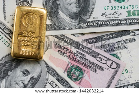 Cast gold bar weighing 250 gram against the background of dollar bills.