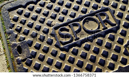 Cast iron manhole with SPQR engraving on white marble flooring in the afternoon sun