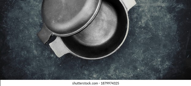 Cast Iron Pot With Cover Or Lid In The Form Of Separate Frying Pan. Top View. Casserole Pot On Black Shabby Background. Flat Lay. New And Clean Cast Iron Cookware.