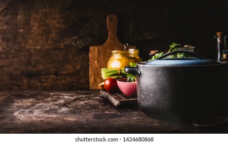 Cast iron pot with fresh herbs, spices and kitchen utensils for tasty cooking on rustic table. Healthy eating. Homemade cooking. Dark. Still life. Food background. Copy space - Powered by Shutterstock