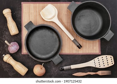 Cast Iron Pot And Frying Pan On Black Isolated Background Top View. Empty Cast Iron Pot And Pan With Cookware Items On Bamboo Rug, Overhead View.