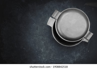 Cast Iron Pot With Half-Open Lid In The Form Of Frying Pan. Top View. Casserole Pot On Black Shabby Background. Flat Lay. New And Clean Cast Iron Cookware.