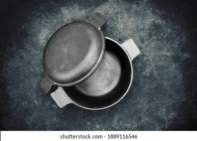 Cast Iron Pot With Lid In The Form Of Separate Frying Pan. Top View. Casserole Pot On Black Shabby Background. Flat Lay. New And Clean Cast Iron Cookware.