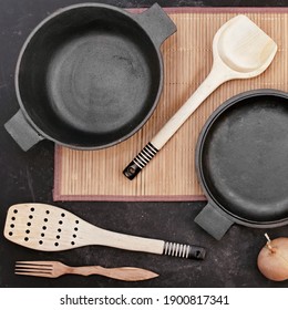 Cast Iron Pot With Lid On Black Isolated Background Top View. Cast Iron Pot And Cookware Items On Bamboo Rug. Empty Cast Iron Pot On Grunge Black Table, Overhead View.