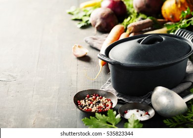 Cast iron pot and vegetables on wooden rustic table. Homemade food, cooking, vegetarian concept