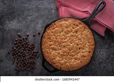 Cast Iron Skillet Chocolate Chip Cookie right out of the overn with loose chocolate chips and kitchen towel on a slate countertop