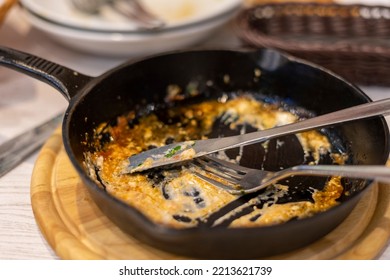 Cast Iron Skillet With Leftover Food And Cutlery.