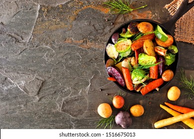 Cast Iron Skillet Of Roasted Autumn Vegetables, Above View Side Border Over A Dark Stone Background