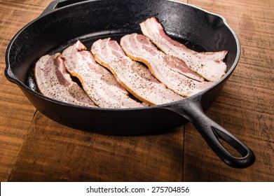 Cast iron skillet with strips of raw bacon ready to fry