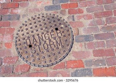 A Cast Iron Storm Drain Cover Set Into A Red Brick Road.