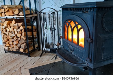 cast iron stove with fire and stacked wood beside