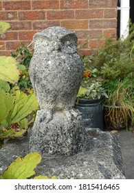Cast stone weathered owl on plinth in back garden in Northamptonshire, UK