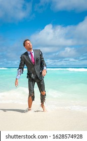 Castaway businessman emerging from tropical sea onto the beach with shredded suit and exhausted expression - Shutterstock ID 1628574928