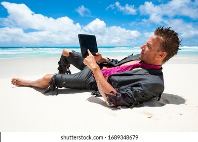 Castaway survivor businessman lying back on a tropical beach in a ragged suit using his tablet computer - Shutterstock ID 1689348679