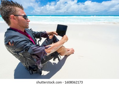 Castaway survivor businessman sitting on a tropical beach in a ragged suit watching his tablet computer - Shutterstock ID 1608062173