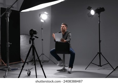 Casting call. Man with script sitting on chair and performing in front of camera in studio