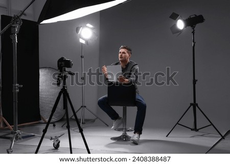 Casting call. Man with script sitting on chair and performing in front of camera in studio ストックフォト © 