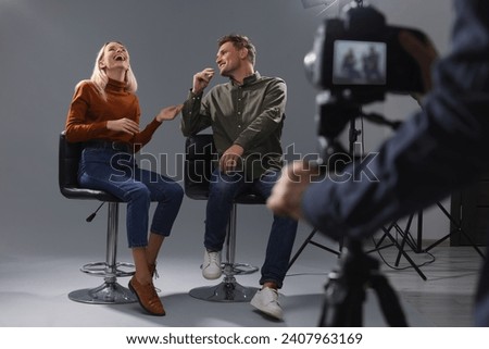 Casting call. Man and woman performing while camera operator filming them against grey background in studio