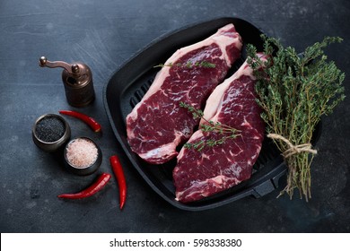 Cast-iron grill pan with two raw striploin steaks of grass-fed beef with seasonings, studio shot