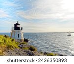 Castle Hill Lighthouse in summer, a beautiful and famous New England light house, Newport, Rhode Island, USA with a sailboat in the distance in Narragansett Bay.