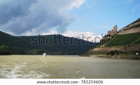 A castle on a hill near the river Rhine along the vineyards and write river ship passing by                          