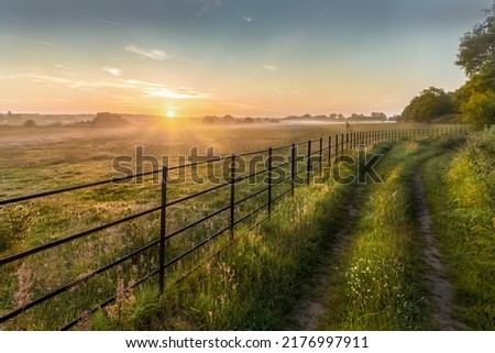 Castle Rising in Norfolk sunrise over metal fence and farm track or footpath. Grass meadows and trees landscape in Summer