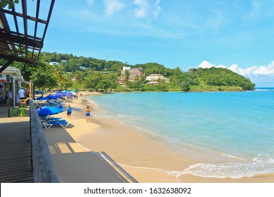 Castries, Saint Lucia - November 23, 2019. Beautiful Day At Vigie Beach - In The Distance, Tourists Sun And Sea Bathing With Green Landscape In The Background, Left - A  Wooden Structure With No Roof.