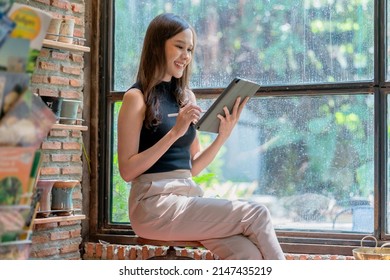 Casual Asia Female Woman Relax Hand Using Tablet Internet Surf Writing Diary Cheerful Smiling While Sittting In Warm Interior Of Cafe Near Big Window,asian Woman Sit On Stool Casual Work In Coffeeshop