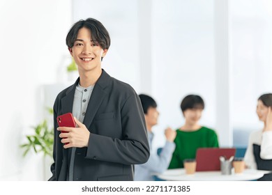 Casual Asian man standing in office with a smart phone. Group meeting. - Shutterstock ID 2271171385