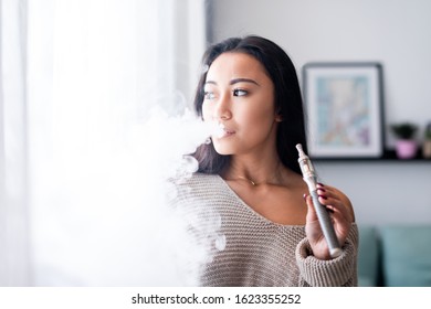 Casual Asian Woman Vaping Electronic Cigarette At Home