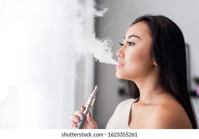 Casual Asian Woman Vaping Electronic Cigarette At Home