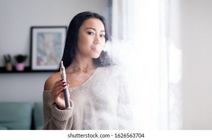 Casual Asian Woman Vaping Electronic Cigarette At Home