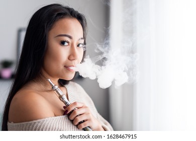 Casual Asian Woman Vaping Electronic Cigarette At Home