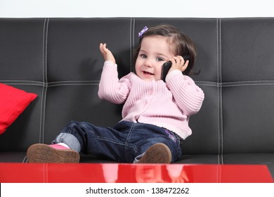 Casual Baby Playing Happy With A Mobile Phone Sitting On A Black Couch At Home