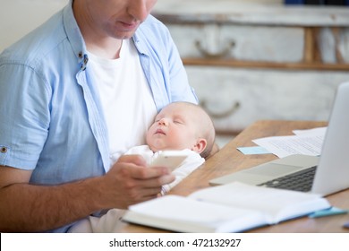 Casual business dad holding sleeping newborn babe while working in home office interior, holding smartphone and looking at screen. Young father using mobile phone and nursing new born child. Close-up - Powered by Shutterstock