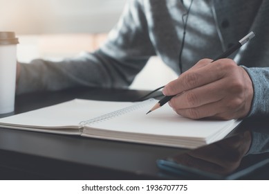 Casual Business Man Hand With A Pencil Writing On Paper Notebook On Wooden Table During Working From Home, Close Up. Student Studying Online Courses Via Digital Tablet And Laptop Computer.