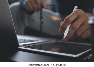 Casual business man sitting at table with stylus pen writing on digital notepad and pointing on digital tablet screen while working on laptop computer in office, close up. Internet technology concept - Shutterstock ID 1704451570