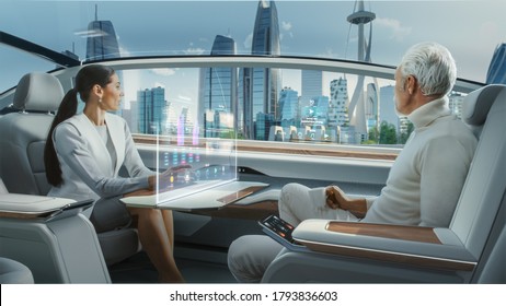 Casual Business Meeting Between Senior Male And Female Inside A Futuristic Driverless Autonomous Car With Augmented Reality Presentation Interface. Self-Driving Van Driving On Downtown City Streets.