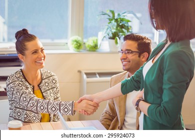 Casual Business People Shaking Hands At Desk And Smiling In The Office