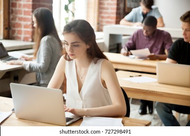 Casual Business Woman Typing On Laptop In Modern Shared Office Surrounded By Coworkers. Young Female Entrepreneur Composing Email, Communicates With Clients Or Business Partners, Setting Appointments.
