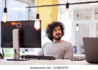 Casual Businessman With Clumsy Hair Working On Desktop Computer In A Modern Coworking Office Space.