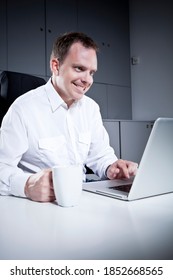 Casual Businessman Sitting By A Computer In A Dark Office Making Pranks Or Bad Things With Evil Look On Face. 