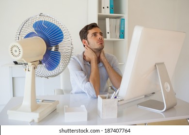 Casual Businessman Sitting At Desk With Electric Fan In His Office