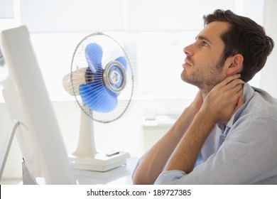 Casual Businessman Sitting At Desk With Electric Fan In His Office