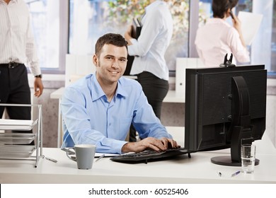 Casual businessman working with computer in office, looking at camera, smiling.? - Powered by Shutterstock