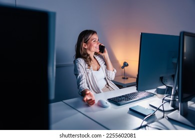 Casual businesswoman having phone conversation using smart phone while working overtime late at night in an office - Shutterstock ID 2255602081