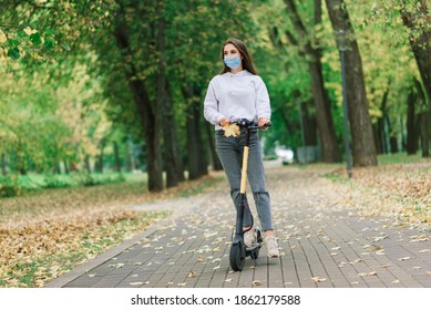 Casual caucasian female wearing protective face mask riding urban electric scooter in city park during covid pandemic. Urban mobility concept. - Powered by Shutterstock